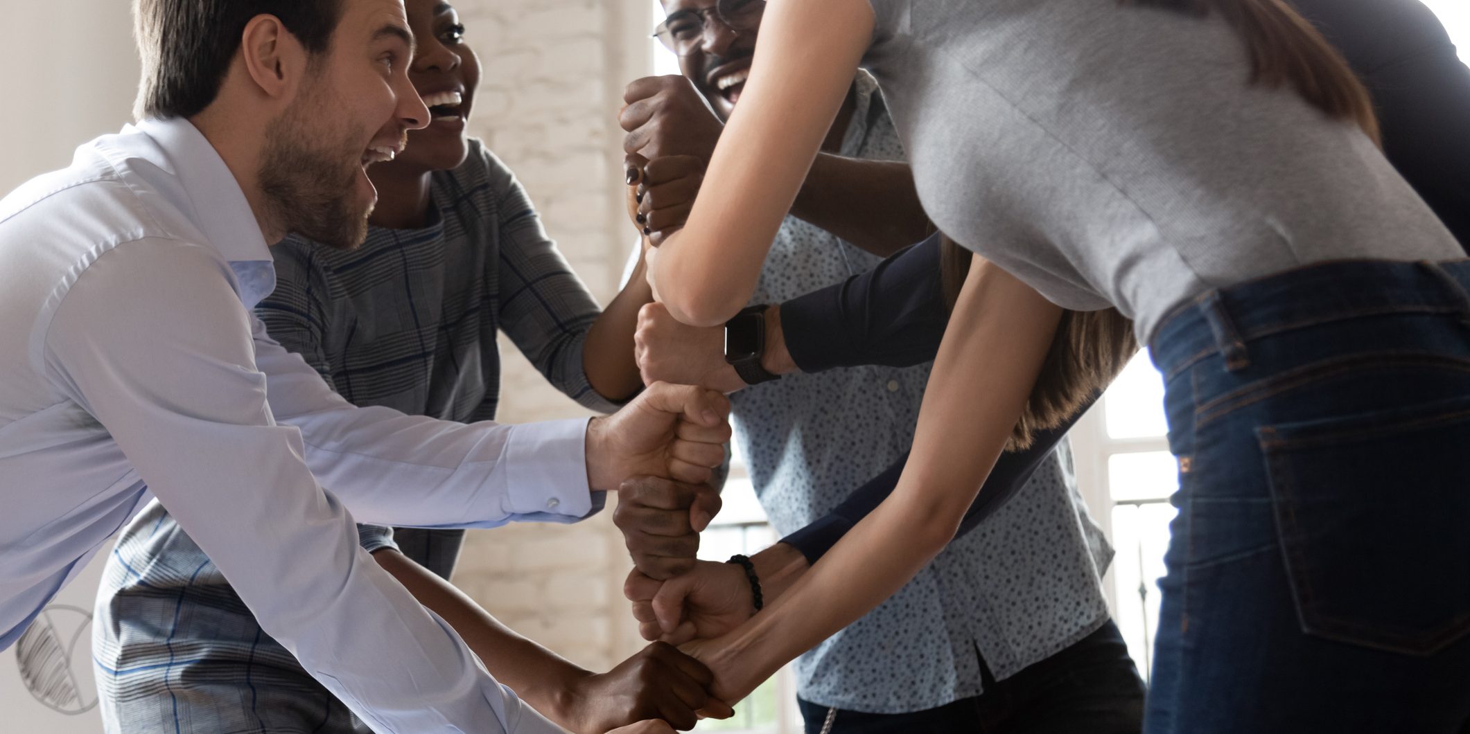Overjoyed happy multiracial business team stacking fists motivated by corporate success, excited international work people group engaged in teambuilding celebrate victory good teamwork result concept